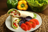 Shaurma without sauce with chicken, pepper, lettuce. Low-calorie roll from pita bread, next to purple basil and slices of tomatoes. Without roasting, raw. In the background pepper and lettuce leaves