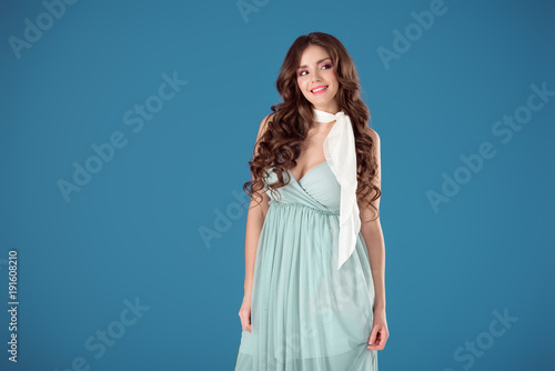 smiling girl in blue dress looking away isolated on blue