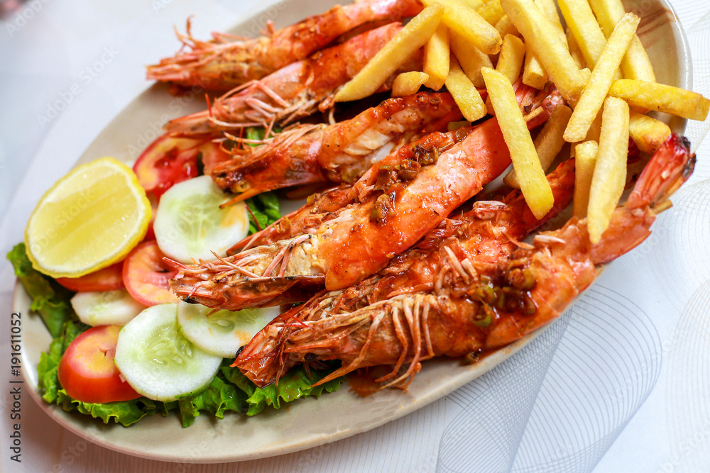 Plate grilled spicy prawn shrimps kebabs, vegetables, french fries with sauces and greens on light background. Plate grilled spicy prawn shrimps kebabs, vegetables, french fries with sauces and greens on light background.