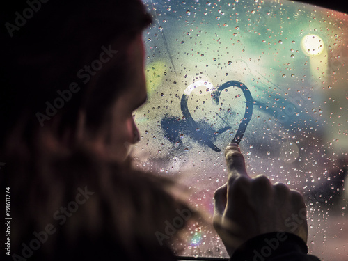 Bild auf Leinwand Side view of romantic man drawing heart on steamy car window against night lights