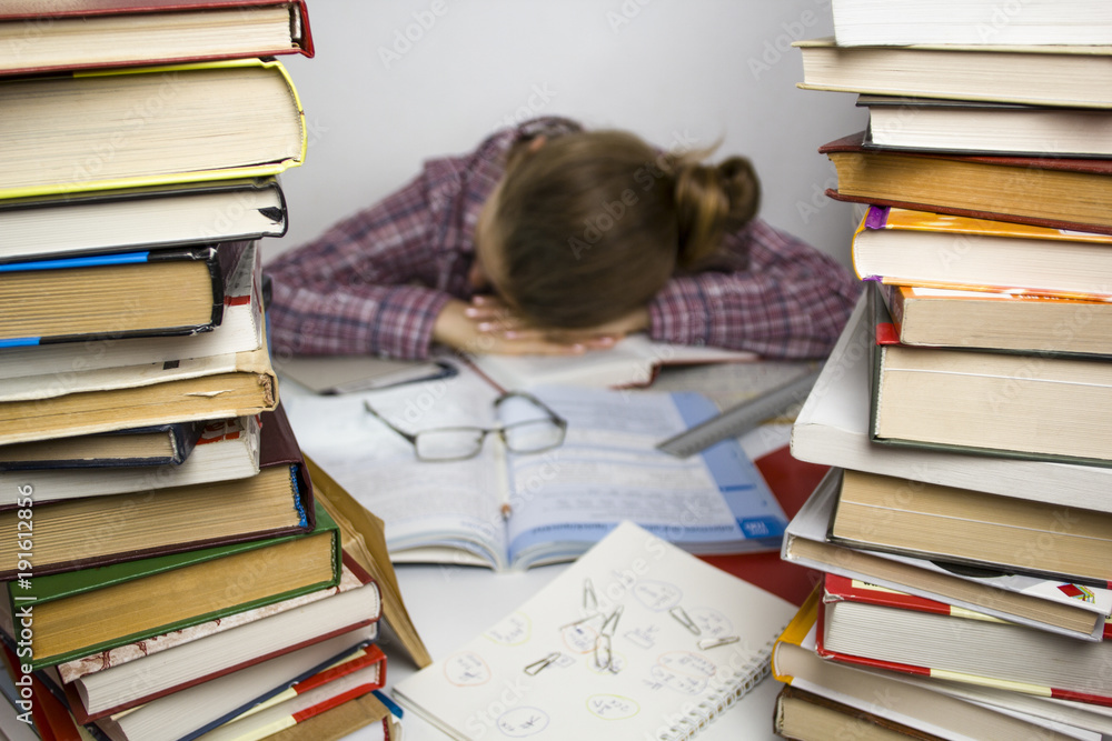 The girl is sleeping surrounded by books. Tired student. The girl is sleeping surrounded by books. Tired student.