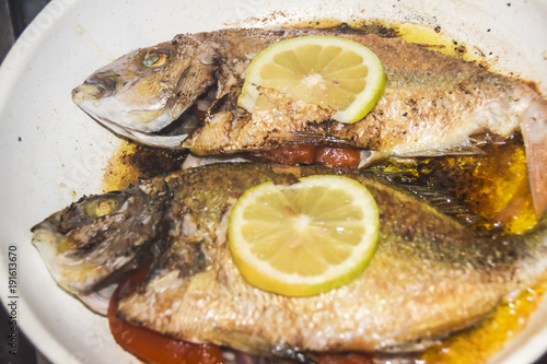 fresh fried baked fish with scales and lemon in a frying pan