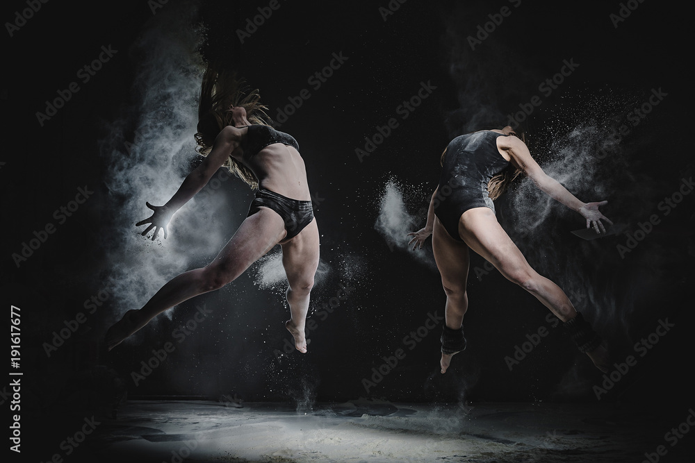Fototapeta Dwie dziewczyny tańczą z mąką w studio na czarnym tle, światła za nimi i ludzie pomagają dziewczynom