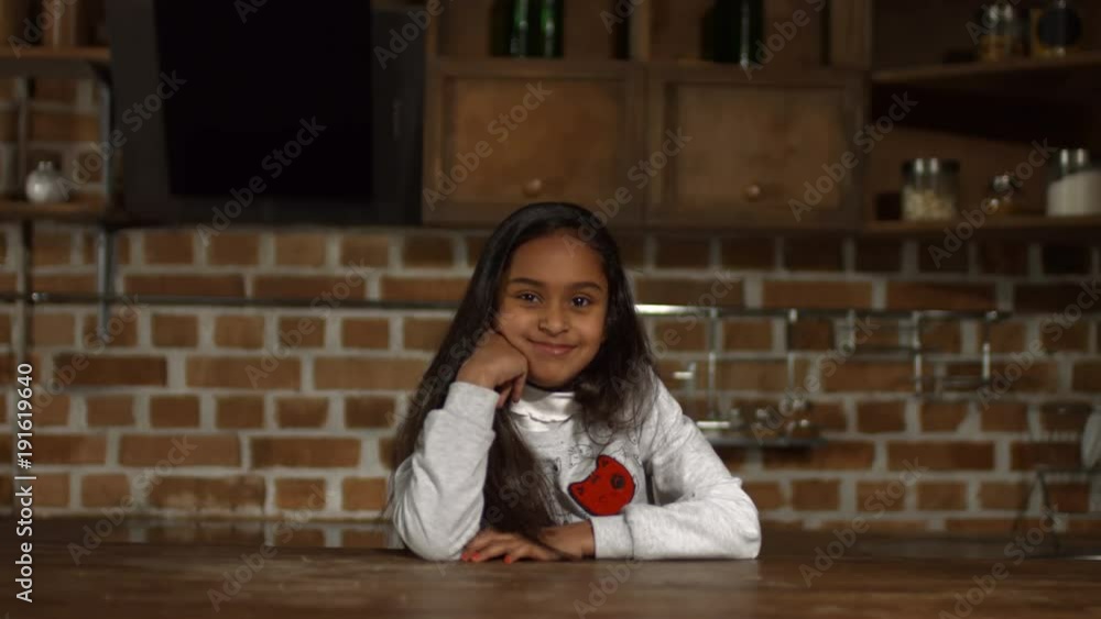 Portrait of cute african american little girl smiling while sitting at kitchen table. Sweet mixed race preteen girl looking at camera with radiant smile , expressing joy and happiness in home interior Portrait of cute african american little girl smiling while sitting at kitchen table. Sweet mixed race preteen girl looking at camera with radiant smile , expressing joy and happiness in home interior