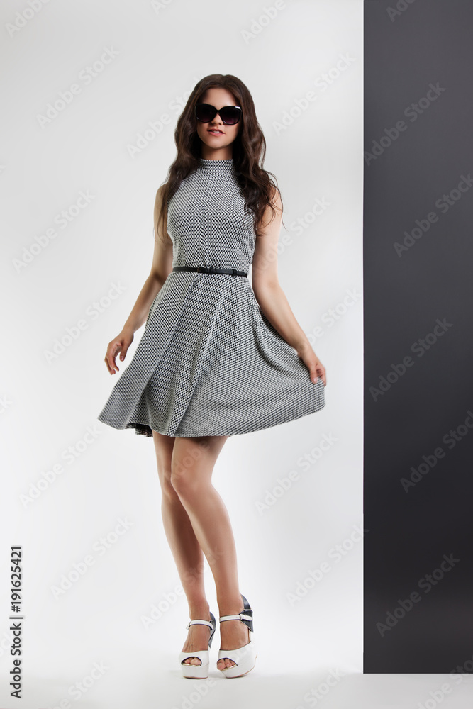fashion portrait of a woman. young beautiful girl in gray dress and sunglasses posing in the Studio. Hand holds on to the dress fashion portrait of a woman. young beautiful girl in gray dress and sunglasses posing in the Studio. Hand holds on to the dress
