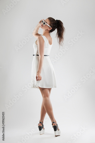 fashion portrait of a woman. a young beautiful girl in a light white dress posing in the Studio. Sunglasses.