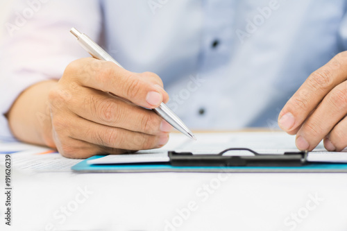 A man's hand holding pen pointing on summary report chart and calculate finance in office.