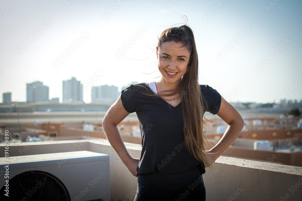 Fototapeta premium Portrait of beautiful smiling young woman posing on rooftop with a city view in the background.