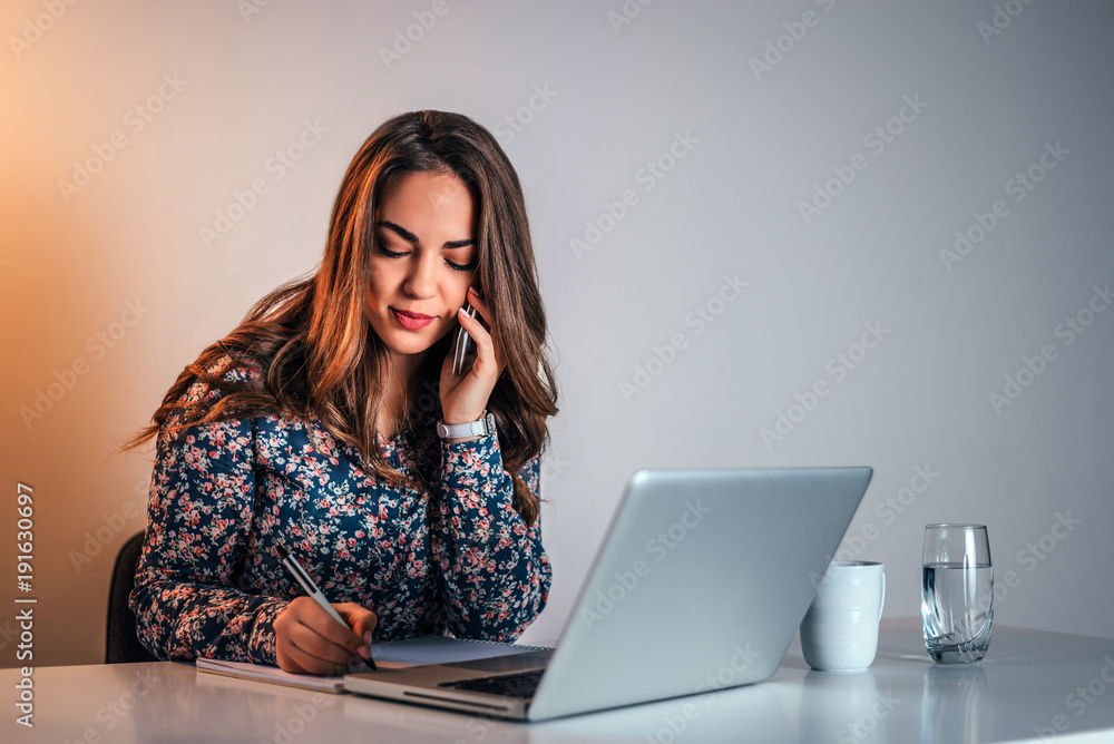 Young woman accountant talking on cell phone and writing notes. Young woman accountant talking on cell phone and writing notes.