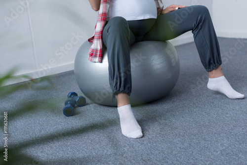 cropped view of pregnant woman sitting on fit ball with dumbbells near