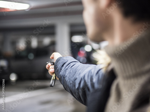 Young trendy man in outerwear standing on parking using alarm remote control.