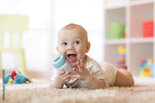 Cute baby boy drinking from bottle. Smiling child is 7 months old.