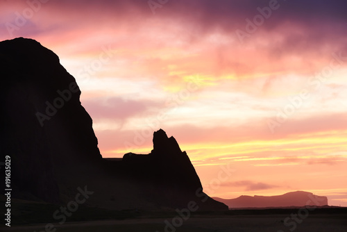 Incredibly beautiful dawn (sunset) on the shore of the Atlantic Ocean. Silhouettes of mountains and red clouds. Iceland. 