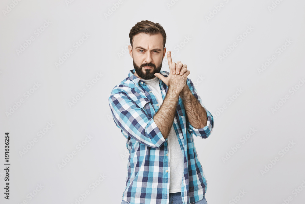 Studio portrait of man fooling around, making gun gesture with confident expression, acting like a spy or secret agent or warrior, standing over gray background. Guy is hunting for huge sales Studio portrait of man fooling around, making gun gesture with confident expression, acting like a spy or secret agent or warrior, standing over gray background. Guy is hunting for huge sales