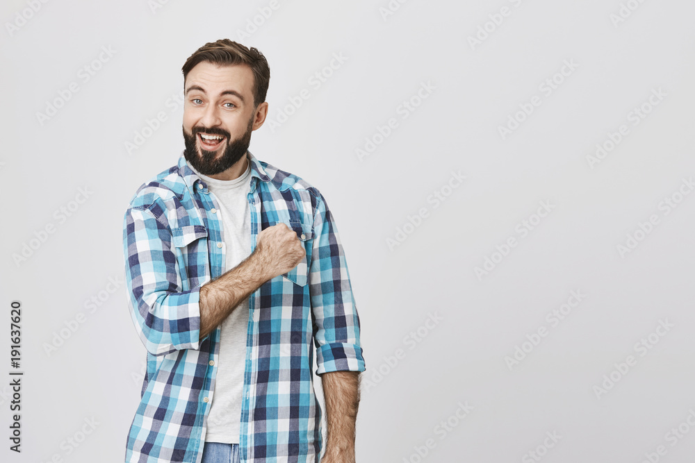 Attractive funny young man with beard and moustache cheerfully lifting his arm and smiling broadly. Plumber took photo in studio to make advertisement of his company, ensuring he can fix everything Attractive funny young man with beard and moustache cheerfully lifting his arm and smiling broadly. Plumber took photo in studio to make advertisement of his company, ensuring he can fix everything