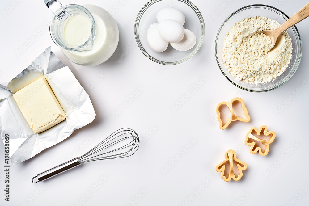Objects and ingredients for baking, plastic molds for cookies on a white background. Flour, eggs, whisk, milk, butter, cream. Top view, space for text Objects and ingredients for baking, plastic molds for cookies on a white background. Flour, eggs, whisk, milk, butter, cream. Top view, space for text