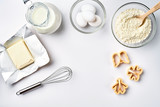 Objects and ingredients for baking, plastic molds for cookies on a white background. Flour, eggs, whisk, milk, butter, cream. Top view, space for text