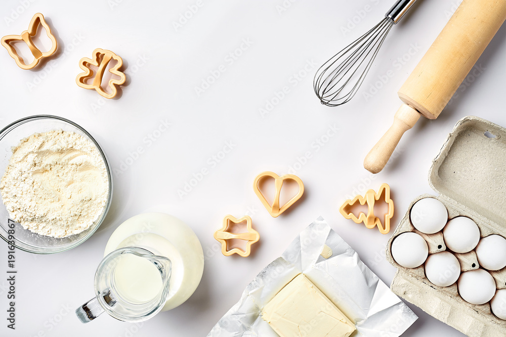 Objects and ingredients for baking, plastic molds for cookies on a white background. Flour, eggs, rolling pin, whisk, milk, butter, cream. Top view, space for text Objects and ingredients for baking, plastic molds for cookies on a white background. Flour, eggs, rolling pin, whisk, milk, butter, cream. Top view, space for text