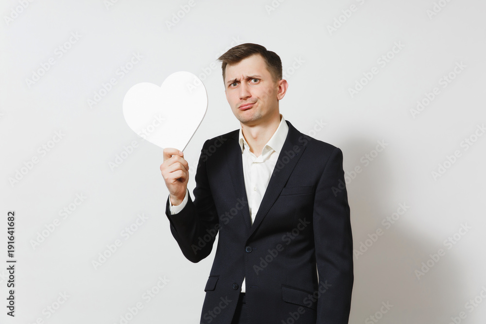 Young stunned shocked upset sad man in suit holding big white heart isolated on white background. Copy space for advertisement. St. Valentine's Day, International Women's Day, birthday holiday concept