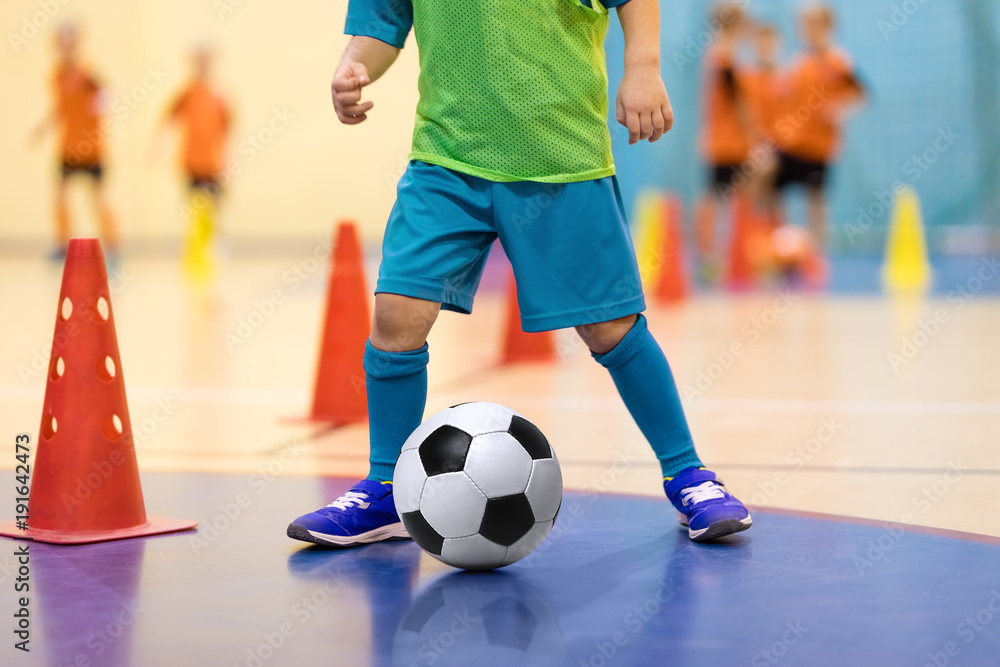 Football futsal training for children. Soccer training dribbling cone drill. Indoor soccer young player with a soccer ball in a sports hall. Player in blue uniform. Sport background.