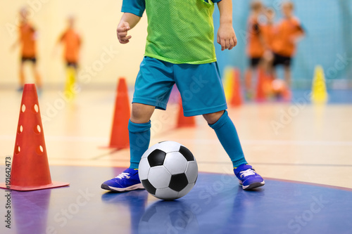 Fototapeta Naklejka Na Ścianę i Meble -  Football futsal training for children. Soccer training dribbling cone drill. Indoor soccer young player with a soccer ball in a sports hall. Player in blue uniform. Sport background.