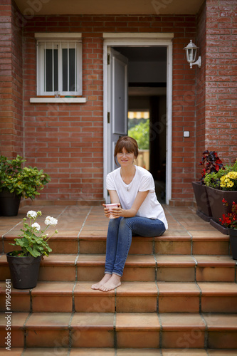 mujer joven con una taza en la entrada de su casa