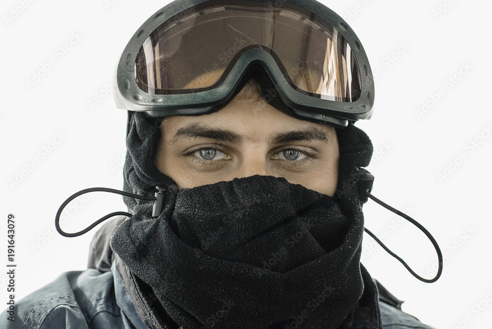 A portrait of a young handsome man (twenty five - thirty five years old) in  a black fleece ski mask and with ski goggles on top of his head. Stock  Photo