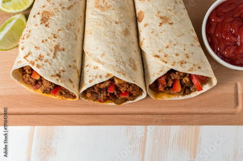 Tasty homemade burrito with vegetables and beef on wooden background.