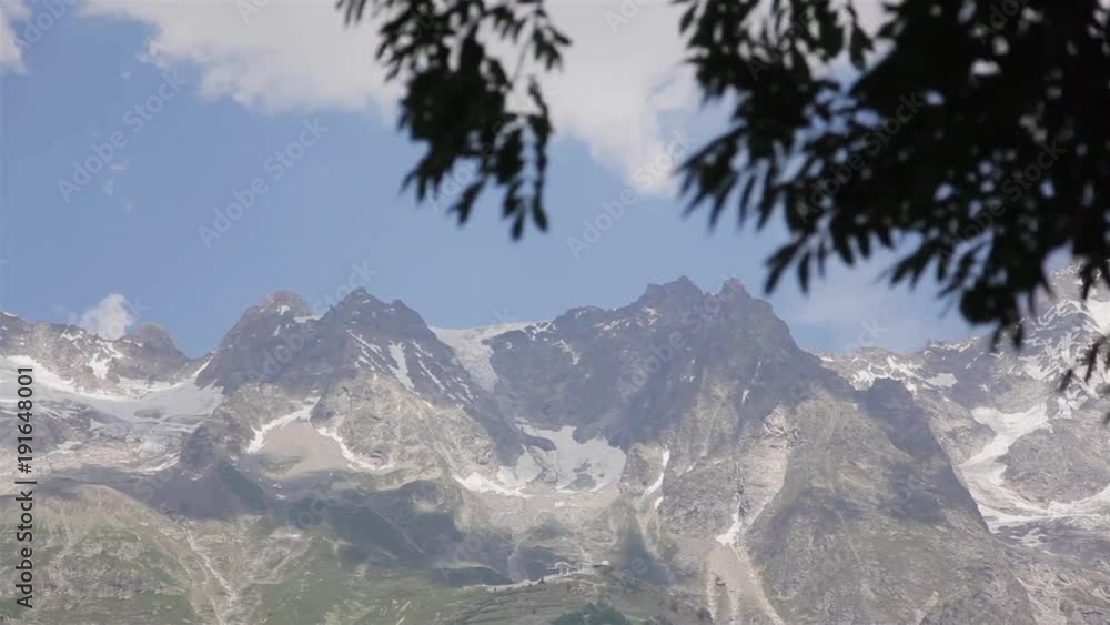 Alps Mont Blanc mountain massif focus view from tree wind. High summer Alpine ridge range seen from Courmayeur town in Aosta Valley sun day. Famous alpinist tourist resort mountaineering destination Alps Mont Blanc mountain massif focus view from tree wind. High summer Alpine ridge range seen from Courmayeur town in Aosta Valley sun day. Famous alpinist tourist resort mountaineering destination