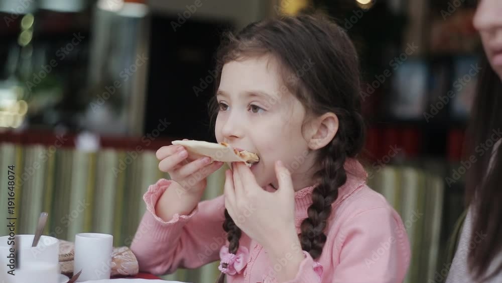 A little girl eats a slice of pizza in the restaurant A little girl eats a slice of pizza in the restaurant