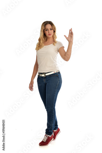 full length portrait of blonde girl wearing white shirt and jeans. standing pose, isolated on white studio background.