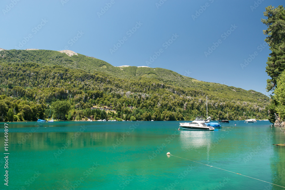 Turquoise lake landscape with moored boats and pine forest