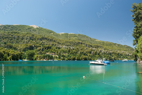 Turquoise lake landscape with moored boats and pine forest