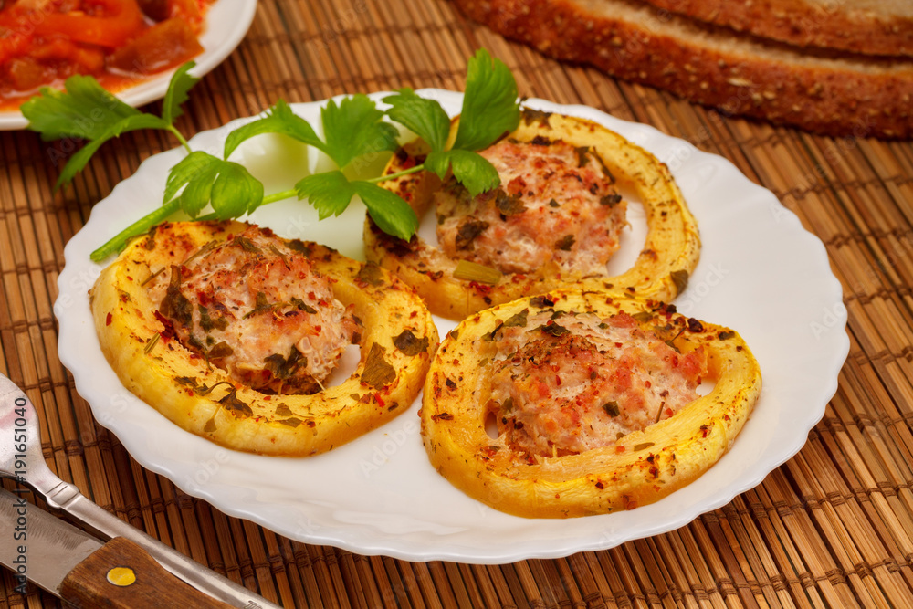 Baked slices of zucchini stuffed with minced meat from turkey, with bread and greens of celery, on a white plate, on a napkin made of bamboo. Baked slices of zucchini stuffed with minced meat from turkey, with bread and greens of celery, on a white plate, on a napkin made of bamboo.