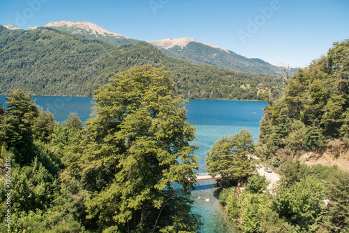 Landscape of a turquoise river rising from a lake and mountains in the background