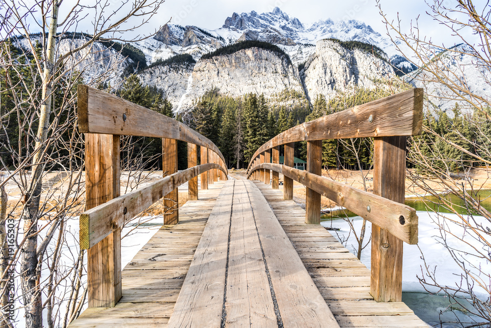 Wooden foot bridge leading over glacial stream to inspiring winter mountains landscape