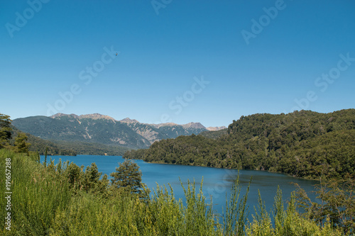 Lake landscape surrounded by mountains and vegetation, with a blue sky