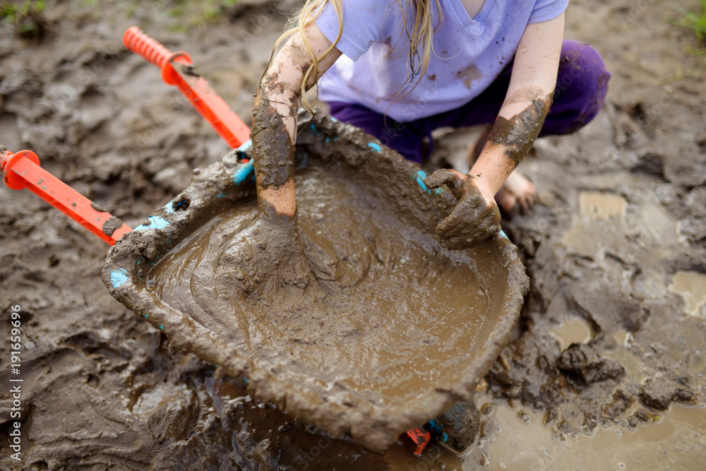 Funny little girl playing in a large wet mud puddle on sunny summer day.  Child getting dirty while digging in muddy soil. Stock Photo | Adobe Stock