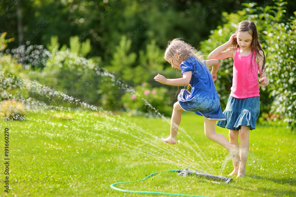 Adorable little girls playing with a sprinkler in a backyard on sunny ...