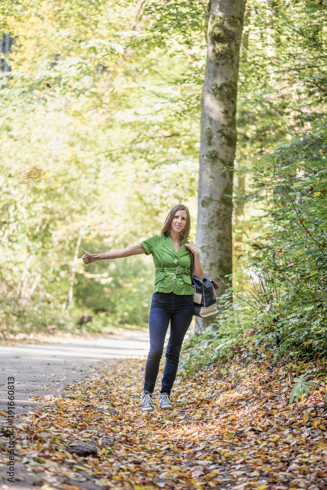 Fototapeta premium Young woman hitchhiker standing in autumn forest
