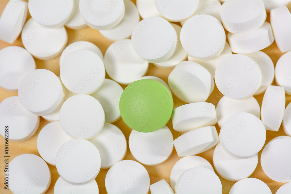 The green pills are on a pile of white pills on a wood background. The green pills are on a pile of white pills on a wood background.