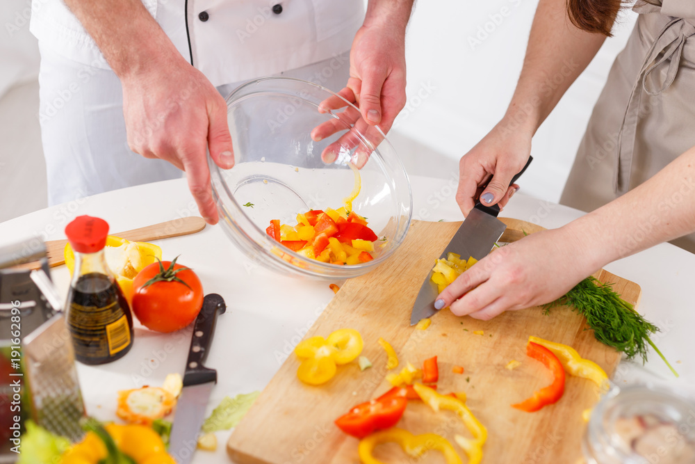 Woman mixing a salad with professional cook in the kitchen
