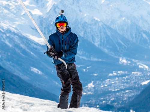 Snowboarder in rainbow goggles and blue helmet using a ski lift - a drag or poma lift with the Chamonix valley in the background