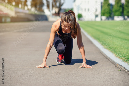 Ready to go! Female athlete on the starting line of a stadium track, preparing for a run. Fitness girl is preparing to run from a low start. Healthy lifestyle.