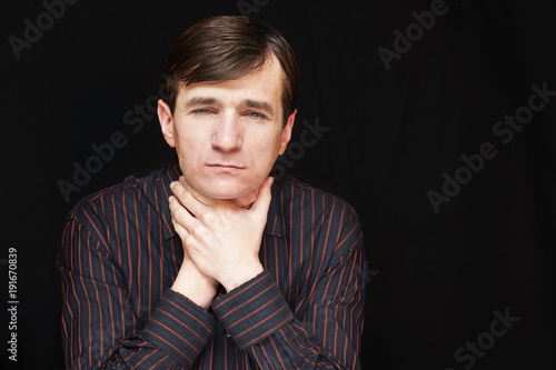 A handsome man in a black shirt holds his neck and сhoke himself on the black background because he has stress