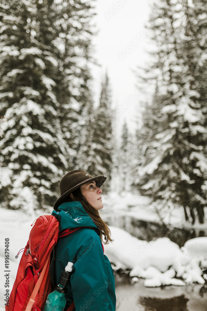 Side view of woman with backpack standing in snow covered forest Side view of woman with backpack standing in snow covered forest