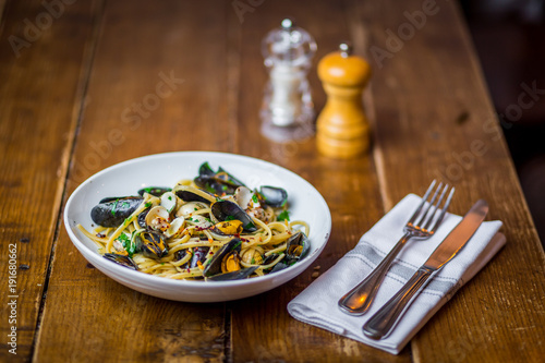 spaghetti vongole italian seafood pasta dish on white plate  on wooden table with fork and knife and salt and pepper