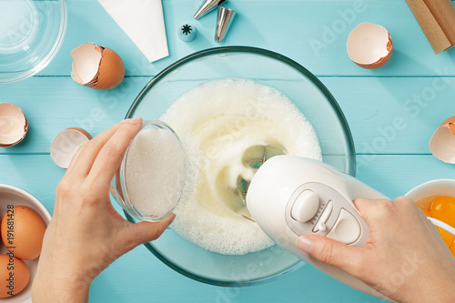 Fotografia, Obraz Female hands add a sugar to the bowl with whipping egg whites with mixer