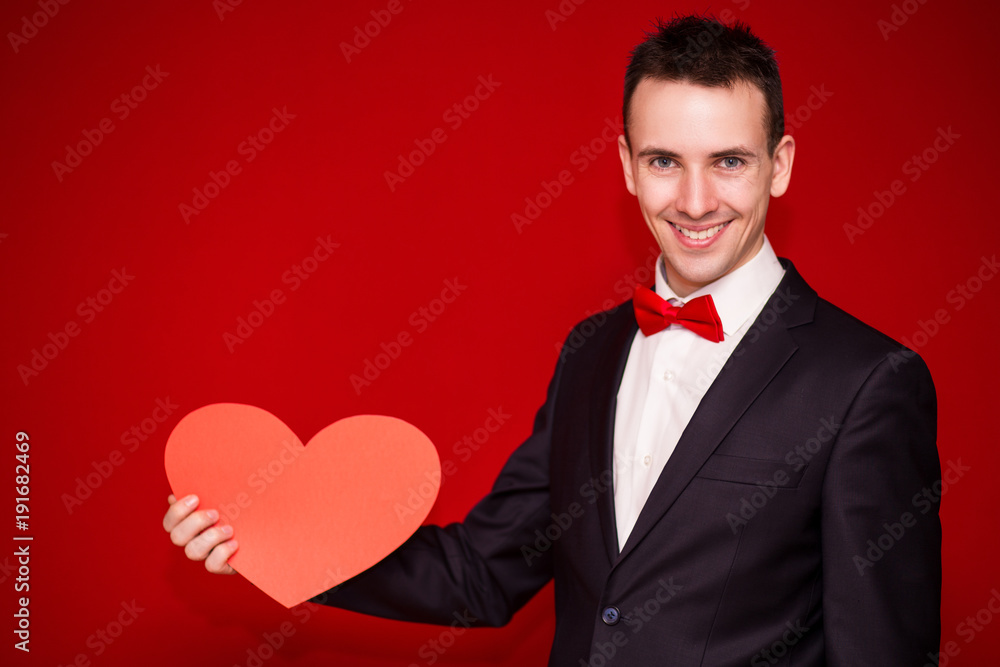 Stylish man in suit hold white paper heart on red backgroundt. Valentines day composition Stylish man in suit hold white paper heart on red backgroundt. Valentines day composition