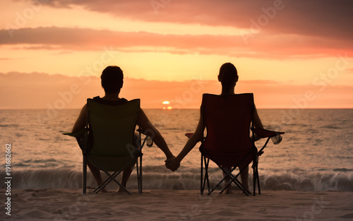 Couple relaxing on the beach watching the sunset holding hands. 